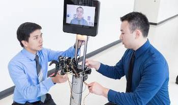people work on robot with human face on screen