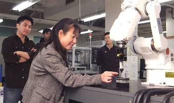 a person holds something near a robot arm with people watching